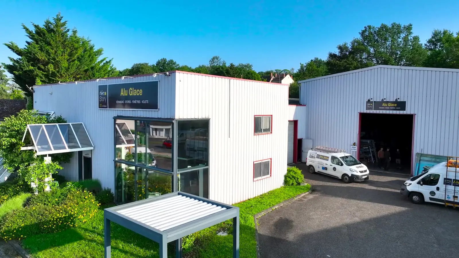 Vue aérienne de l’agence Alu Glace de Vierzon : bâtiment blanc à l’enseigne Alu Glace, entrée vitrée, pergola à lames, camionnettes devant l’atelier