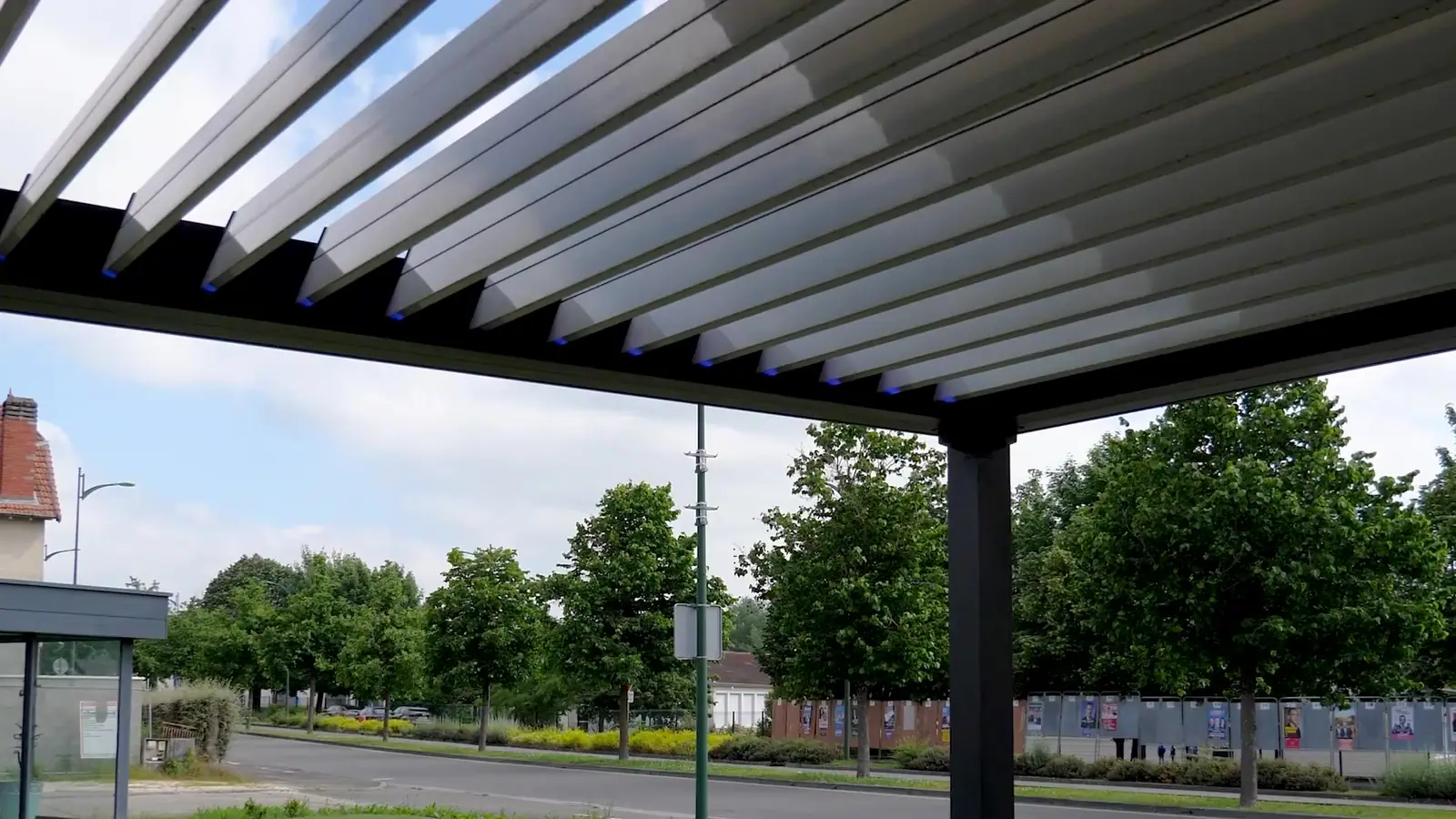 Lames orientables d’une pergola grise, ouvertes, arbres et ciel en arrière-plan